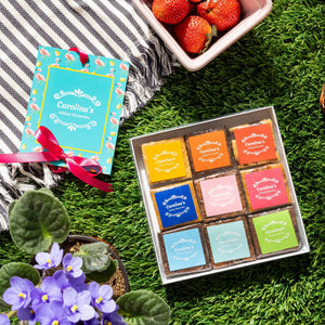 Box of colorful chocolates on grass with strawberries and a card