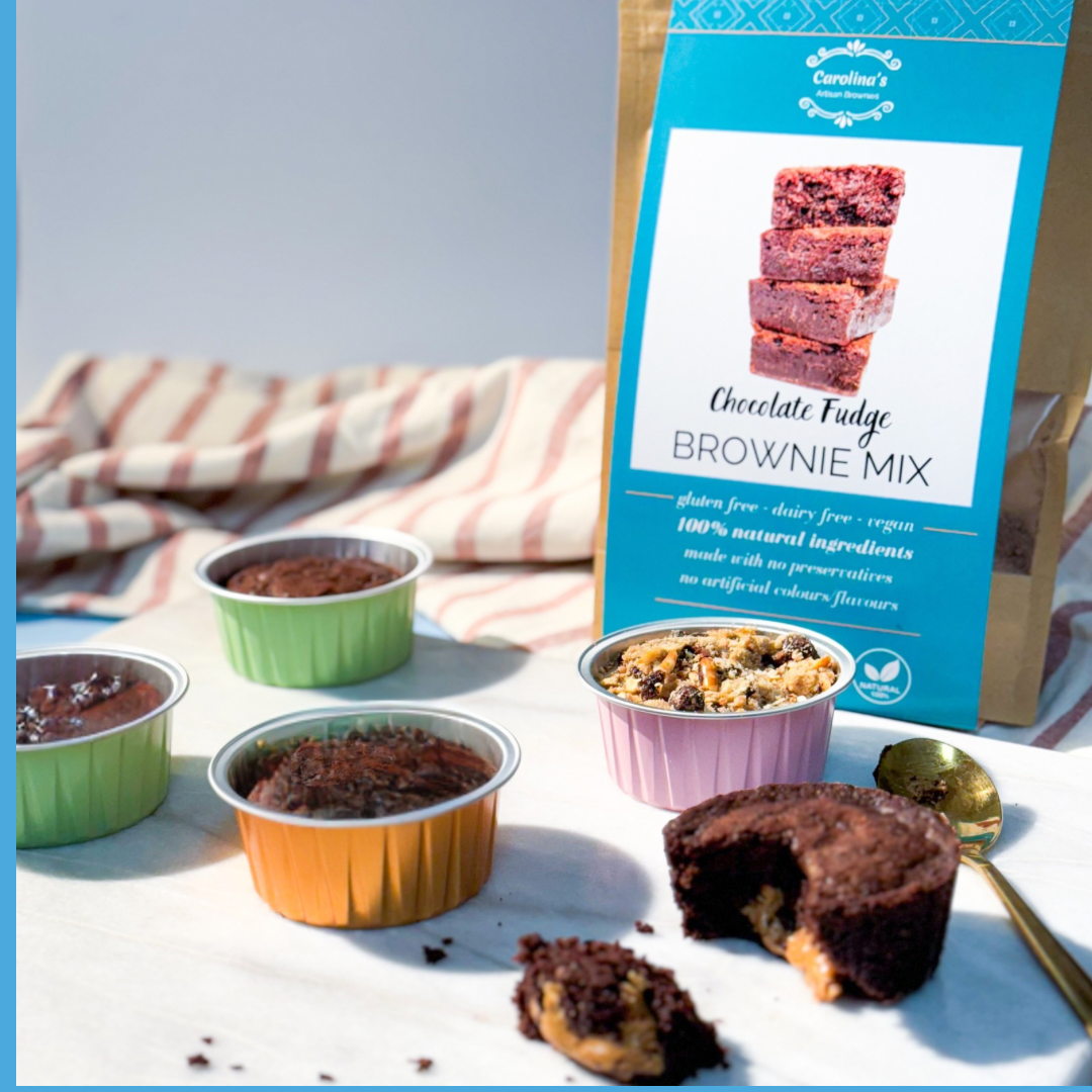 A packaged brownie mix labeled 'Chocolate Fudge Brownie Mix' with prepared brownies in baking dishes and a spoon in the foreground.
