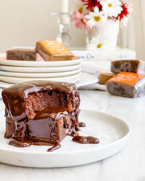two brownies on a white plate, with chocolate sauce on top, the one on top is partially eaten with tooth marks. scattered brownies and a vase of flowers in the background 