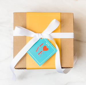 A gift box with a yellow sleeve and a blue  'With Love' tag, with a white ribbon on top.